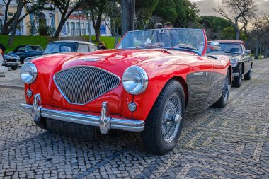 Lizbon, Portekiz - 20 Ocak 2024: 2 tonluk Reno kırmızısı ve siyah Austin-Healey 100 model üstü açık spor araba kaldırım yolunda park edilmiş. Kırmızı kadife ve deri, tahta direksiyon, katla