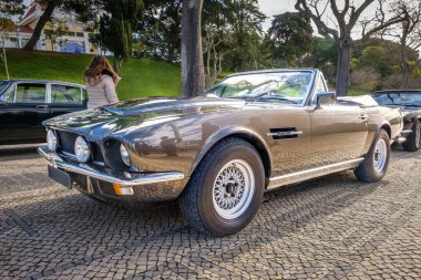 Lizbon, Portekiz - 20 Ocak 2024: Klasik kahverengi Aston Martin V8 Vantage Grand Tourer parke taşlı bir yolda park etmiş, İngiltere 'nin ilk süper arabası, 2 kapılı üstü açık spor araba