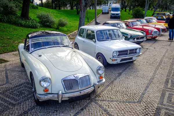 stock image Lisbon, Portugal - Jan 20, 2024: A row of vintage cars of MG and Mini Cooper brand and others parked on cobblestone driveway near green park. MGA, 1973 Morris Mini Clubman, MGC Roadster, MGA TWIN CAM