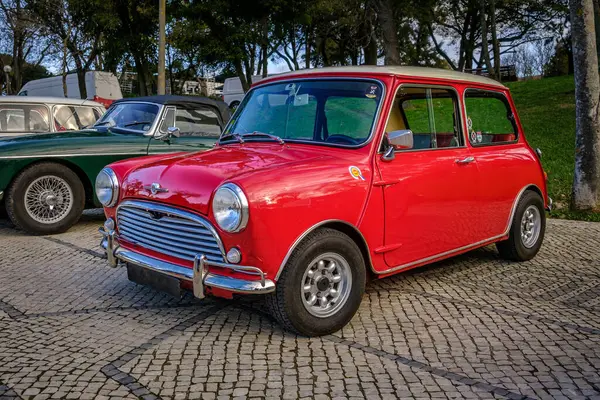 stock image Lisbon, Portugal - Jan 20, 2024: A classic red Mark I Mini or Austin Mini Super-Deluxe car with chrome detailing is parked on a cobblestone path near green park. 