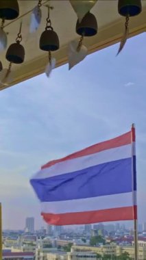 Altın yapraklı Budist çanları, Tayland uyruklu ve güçlü rüzgarda dalgalanan Tayland kraliyet bayrakları ve arka planda Bangkok şehir manzarası. Açık mavi gökyüzü, bulutlar, akşam sisi, Tayland, semboller, din