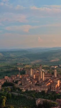 San Gimignano 'nun ünlü kulelerinin, Toskana bölgesinin şafak vakti Toskana tepelerinin, bir UNESCO miras alanı olan ortaçağ İtalyan gökdelenleri şehrinin havadan aşağı veya kule şeklinde yakın görüntüsü. Alçak güneş