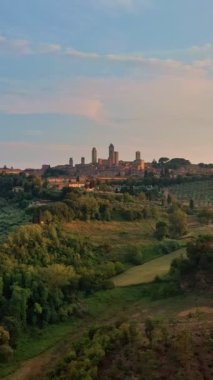 San Gimignano 'nun ünlü kulelerinin, Toskana bölgesinin şafak vakti Toskana tepelerinin, bir UNESCO miras alanı olan ortaçağ İtalyan gökdelenlerinin hava aracı görüntüsü. Alçak güneş, akşam