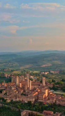 San Gimignano 'nun ünlü kulelerinin, Toskana bölgesinin şafak vakti Toskana tepelerinin, bir UNESCO miras alanı olan ortaçağ İtalyan gökdelenleri şehrinin hava ve çember veya yörünge drone görüntüsü. Alçak güneş