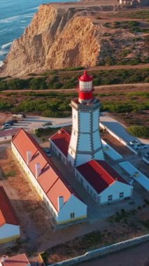 Gün batımında Cabo Espichel ya da Cape Espichel 'deki deniz fenerinin insansız hava aracı görüntüsü. Atlantik Okyanusu kıyısı, Sesimbra, Portekiz. Yörünge, parallaks, yüksek uçurumlar, Portekiz mimarisi, günbatımı yazı