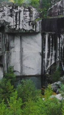 İHA ileri uçar, aşağı eğilir ve terk edilmiş mermer ocağı, Apuan Alps dağları, Carrara, İtalya 'daki küçük yağmur suyu havuzuna yönelir. Siyah ve beyaz yaşlanmış ve yıpranmış ünlü Carrara 'nın kesilmiş blokları