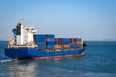 Deniz limanı yakınlarındaki limanda seyir halindeki konteynırlarla dolu modern mavi bir yük gemisi. Küresel ticaret, deniz lojistiği, kargo, uluslararası yük. 