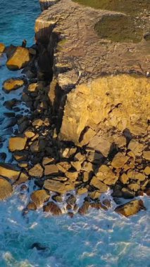 İnsansız hava aracı gün batımında yüksek uçurumlardan ve deniz dalgalarından uzak durur. Okyanus dalgalarının çekim gücü kayalık kıyılarda kırılır ve geri çekilir. Yaz günbatımı sisi, büyük taşlar, insanların eğlenmesi.