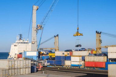 Large port crane loading car onto bulk carrier at shipping port. Colorful shipping containers stacked, ship-to-shore crane, shipment, reach stacker in operation, vehicles on top of freight containers clipart