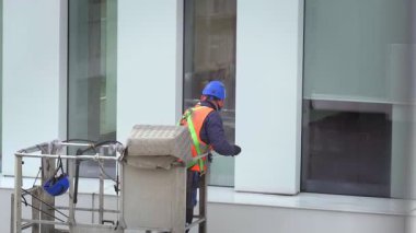 Güvenlik kemeri takan işçiler ofis binasının duvarlarını, panellerini ve pencerelerini boyunda paspasla sildiler. Basınç makinesini kullandıktan sonra vinç beşiğinde ya da hava platformunda durdular. Yakın çekim