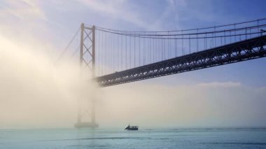 Güneşli bir günde Tagus Nehri, Lizbon, Portekiz üzerindeki sisli 25 Nisan tarihli ikonik köprünün güzel zaman çizelgesi. Üzerinde sis olan asma köprü, köprüde trafik, güneş ışığı ve mavi gökyüzü, sakin