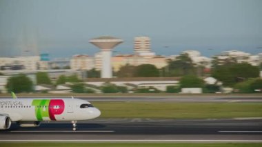 Lizbon, Portekiz - 3 Nisan 2024: TAP Air Portugal Airbus A321neo uçak pisti Lizbon Havalimanı 'nda taksicilik yapıyor, hangarları, havaalanı altyapısı, arka planda açık mavi gökyüzü bulunuyor. Güneşli bir gün, Ryanair