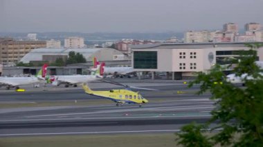 Lizbon, Portekiz - 9 Mayıs 2024: INEM 'in el kamerası görüntüsü, ulusal tıbbi acil durum enstitüsü, Lizbon Humberto Delgado havaalanından kalkan sarı kurtarma helikopteri, otobüsler, kentsel binalar