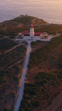 Gün batımında Cabo Espichel ya da Cape Espichel 'deki deniz fenerinin insansız hava aracı görüntüsüne yaklaşıyoruz. Atlantik Okyanusu kıyısı, Sesimbra, Portekiz. Geniş görüş, yakınlaşma, çekilme, yüksek uçurumlar, Portekiz mimarisi