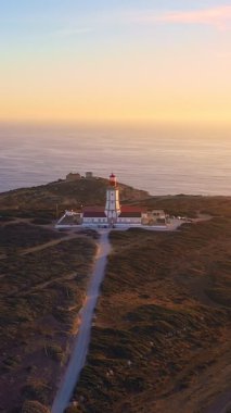 Gün batımında Cabo Espichel ya da Cape Espichel 'deki deniz fenerinin insansız hava aracı görüntülerini geri çekiyoruz. Atlantik Okyanusu kıyısı, Sesimbra, Portekiz. Uç git, parallax, yüksek uçurumlar, Portekiz mimarisi