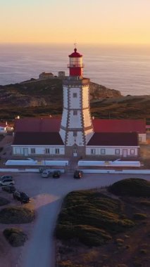 Gün batımında Cabo Espichel ya da Cape Espichel 'deki deniz fenerinin insansız hava aracı görüntülerini geri çekiyoruz. Atlantik Okyanusu kıyısı, Sesimbra, Portekiz. Uç git, parallax, yüksek uçurumlar, Portekiz mimarisi