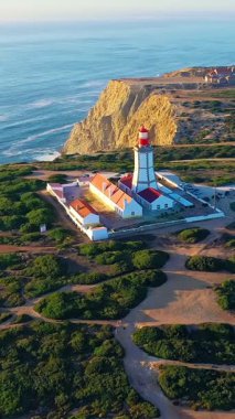 Gün batımında Cabo Espichel ya da Cape Espichel 'deki deniz fenerinin insansız hava aracı görüntüsüne yaklaşıyoruz. Atlantik Okyanusu kıyısı, Sesimbra, Portekiz. Çek, yüksek uçurumlar, Portekiz mimarisi, gün batımı yaz manzarası.