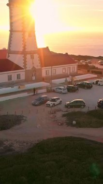 Cabo Espichel ya da Cape Espichel 'deki deniz fenerinin havadan çekilmiş havadan çekilmiş görüntülerini ufuk çizgisinde güneşin batışına doğru çevirerek. Atlantik Okyanusu kıyısı, Sesimbra, Portekiz. Parallaks, yükseliş, yüksek kayalıklar