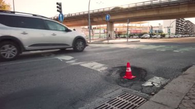 Arabalar ve otobüsler şehir caddesinde trafik konileri ve tali yol işaretleriyle işaretlenmiş büyük çukurlarla, üstgeçitteki araçlarla yol alırlar. Kentsel altyapı sorunları, yol güvenliği, yoğun trafik saatleri, sokak tamiratları, trafik aksaması, sıcak hava dalgası, asfalt erimesi, yaz mevsimi