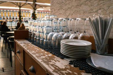 Temiz bardaklar, çatal bıçaklar, Portekiz, Lizbon 'daki açık kafede aşınmış ahşap tezgahların üzerine istiflenmiş tabaklar. Rahatlamış yemek atmosferi, oturanlar, şemsiyeler, tarihi şehir meydanı, seyahat yerleri, seçici odak, bulanık arka plan