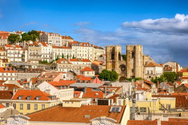 Lizbon, Portekiz 'in panoramik manzarası, ikonik Se Katedrali ile tarihi Alfama bölgesi, kırmızı kiremitli çatıları olan geleneksel Portekiz mimarisi ve açık mavi gökyüzü ve bulutlu güneşli bir günde renkli şehir manzarası. Meşhur seyahat yeri