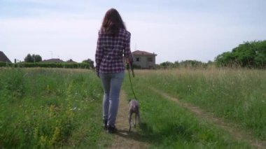 Tarla yolunda tazı köpeğiyle yürüyen bir kadın.