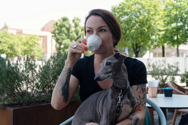 年轻女人带着她的狗坐在街边友好的自助餐厅里喝咖啡 — 图库照片