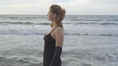 Rıhtımda, bulutlu gökyüzünde poz veren uzun siyah elbiseli bir manken.