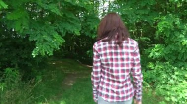 Genç kadın kareli gömlek ve kot pantolon giyiyor yaz ormanlarında tazı köpeğiyle yürüyor.