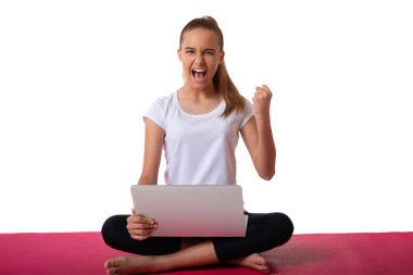Duygusal sportif genç kadın pembe yoga minderinde oturmuş lotus pozu veriyor. Evet bağır. Yumruk at ve dizüstü bilgisayar kullan.