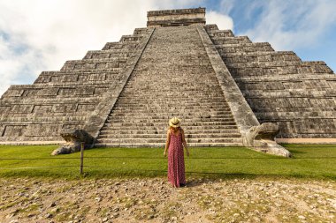 Meksika, Yucatan 'daki Chichen-Itza piramidinin önünde şapka ve kırmızı elbise giyen kadın.