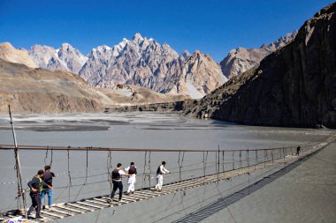  Passu dağları manzaralı Hussaini asma köprüsünden geçen insanlar, Yukarı Hunza, Pakistan 'daki Karakoram Otoyolu