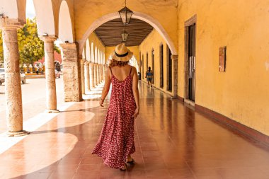 Meksika 'nın Valladolid şehrinin tarihi bölümünde kemer koridorunda yürüyen şapkalı genç bir kadın.