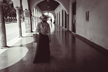 Meksika 'nın Valladolid şehrinin tarihi bölümünde kemer koridorunda yürüyen şapkalı genç bir kadın.