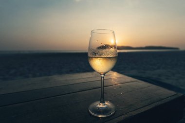 Kumsalda gün batımına karşı sisli bardakta beyaz şarap