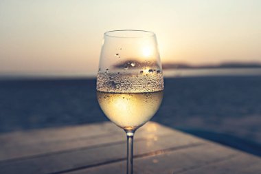Kumsalda gün batımına karşı sisli bardakta beyaz şarap