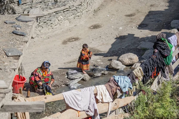 stock image Kalash woman wearing traditional clothes making laundry with her child near her house in Kalash village, Gilgit, Pakistan