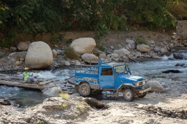 Pakistan dağlarında nehri geçen off-road arabası.