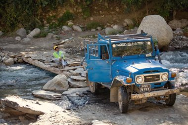 Pakistan dağlarında nehri geçen off-road arabası.