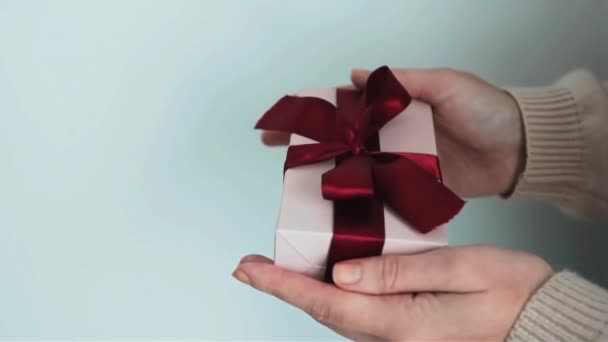 贈り物を保持する女性の手 ソフトピンク色の赤いリボンを閉じます — ストック動画