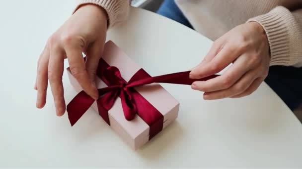 女人的手打开礼物的包装 把柔软的粉红缎带紧紧地系在一起 — 图库视频影像