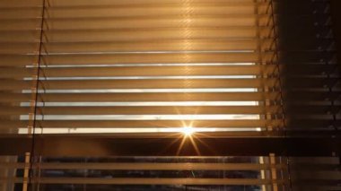 Güneşin ışınları perdelerin arasından parlıyor.