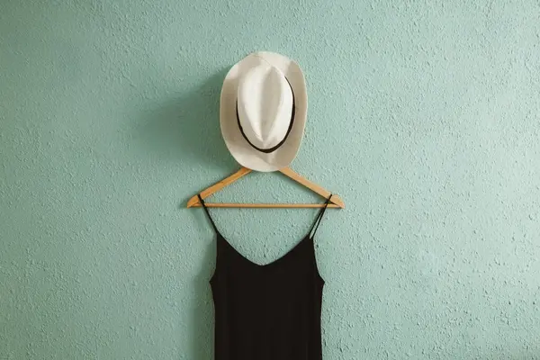 stock image Black dress and a summer hat on a hanger with rough old wall background