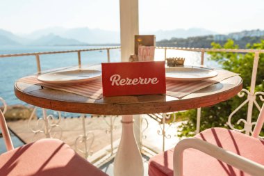 Masadaki rezervasyon tabelası. Kırmızı, güneşli, kafe çiçekleri süslenmiş.