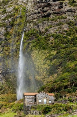 Small stone house in the mountains with waterfall next to it at Flores islamd Azores Portugal clipart