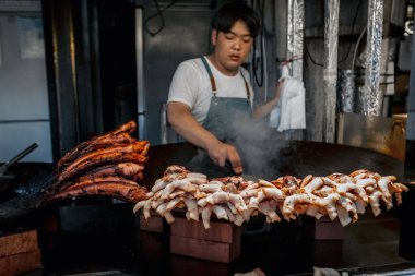 Kore 'li adam Jeju, Güney Kore' de sokak gıda pazarında kalamar ve ahtapot pişiriyor.