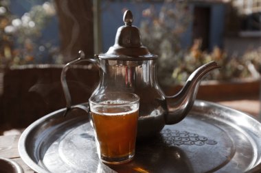 Çay demliği ve bir fincan çay tepside arka planda bir kedi koşuyor.