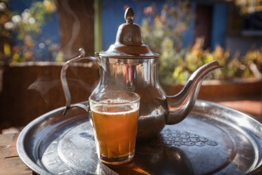 Çay demliği ve bir fincan çay tepside arka planda bir kedi koşuyor.