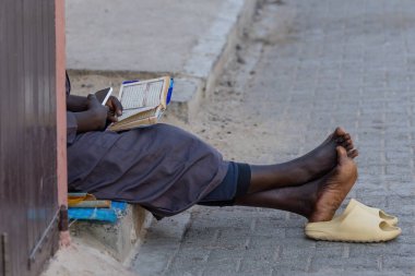 Kaldırımda oturan ve Senegal Afrika kitabını okuyan adam.
