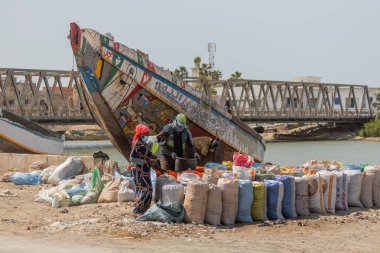 İnsanlar St. Louis Senegal limanındaki çöpleri ahşap bir köprüye ve arka plandaki tekneye ayırıyor.